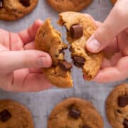 Hands holding up a toffee chocolate chip cookie and breaking it in half.