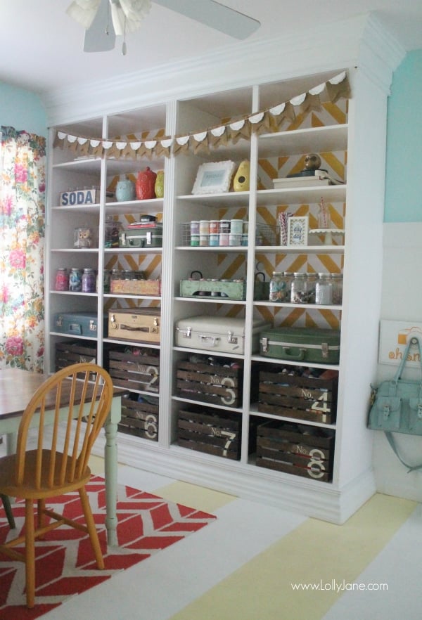 Built in shelving storage that uses painted crates and old luggage to showcase and office supplies organization perfect for organizing your craft room efficiently.