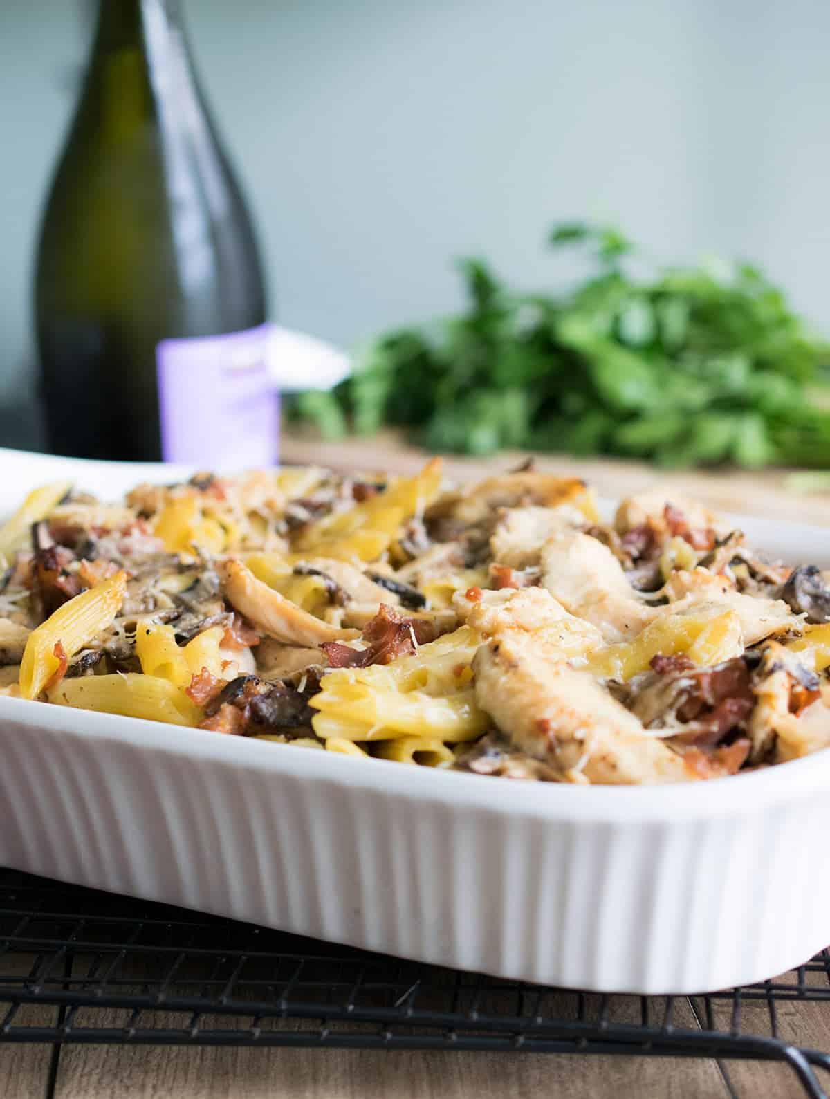 Creamy baked chicken marsala pasta in white bakeware with prosciutto, mushrooms, and parmesan cheese on top.