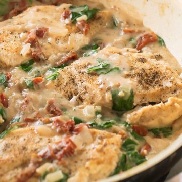 Keto Tuscan Chicken Recipe with Coconut Milk. Spinach, seasoned chicken and sun-dried tomatoes in a pan.