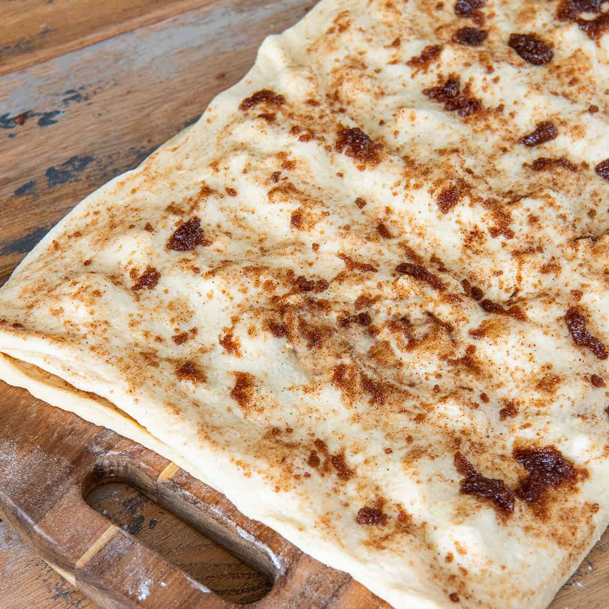 Cinnamon sugar mixture being gently spread onto double layer cinnamon rolls.
