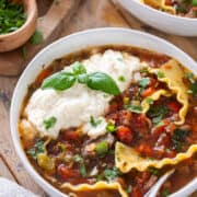 Crockpot lasagna soup in a bowl with ricotta cheese and fresh basil on top.