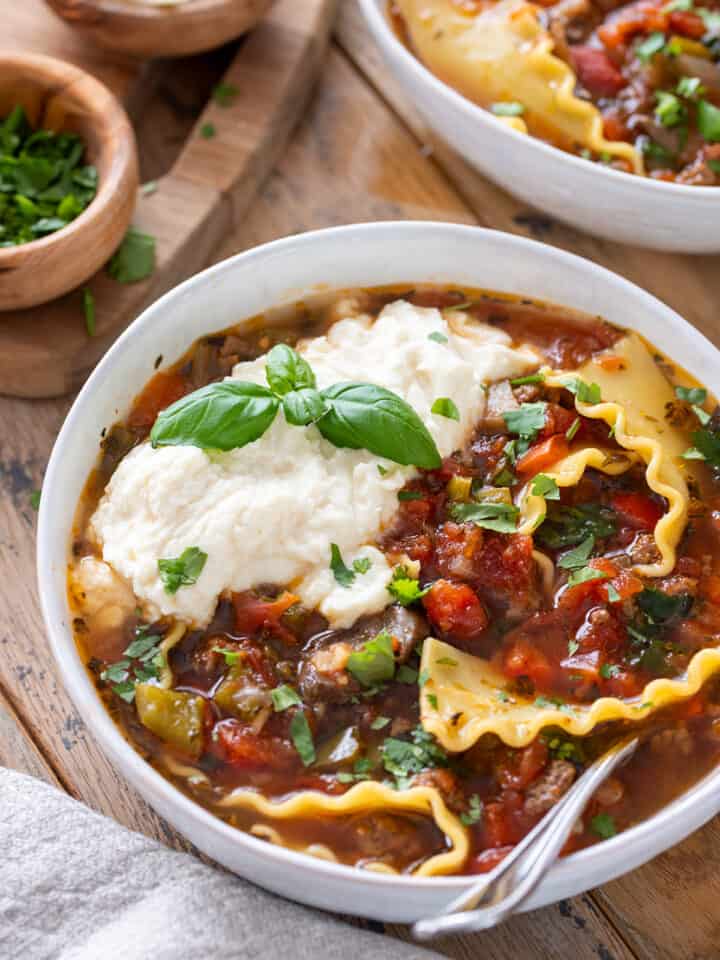Crockpot lasagna soup in a bowl with ricotta cheese and fresh basil on top.