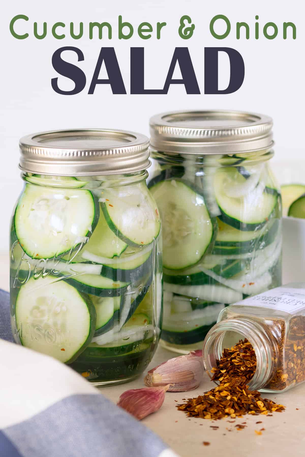 Two mason jars filled with cucumber salad in vinegar on wooden table next to sliced cucumbers. 