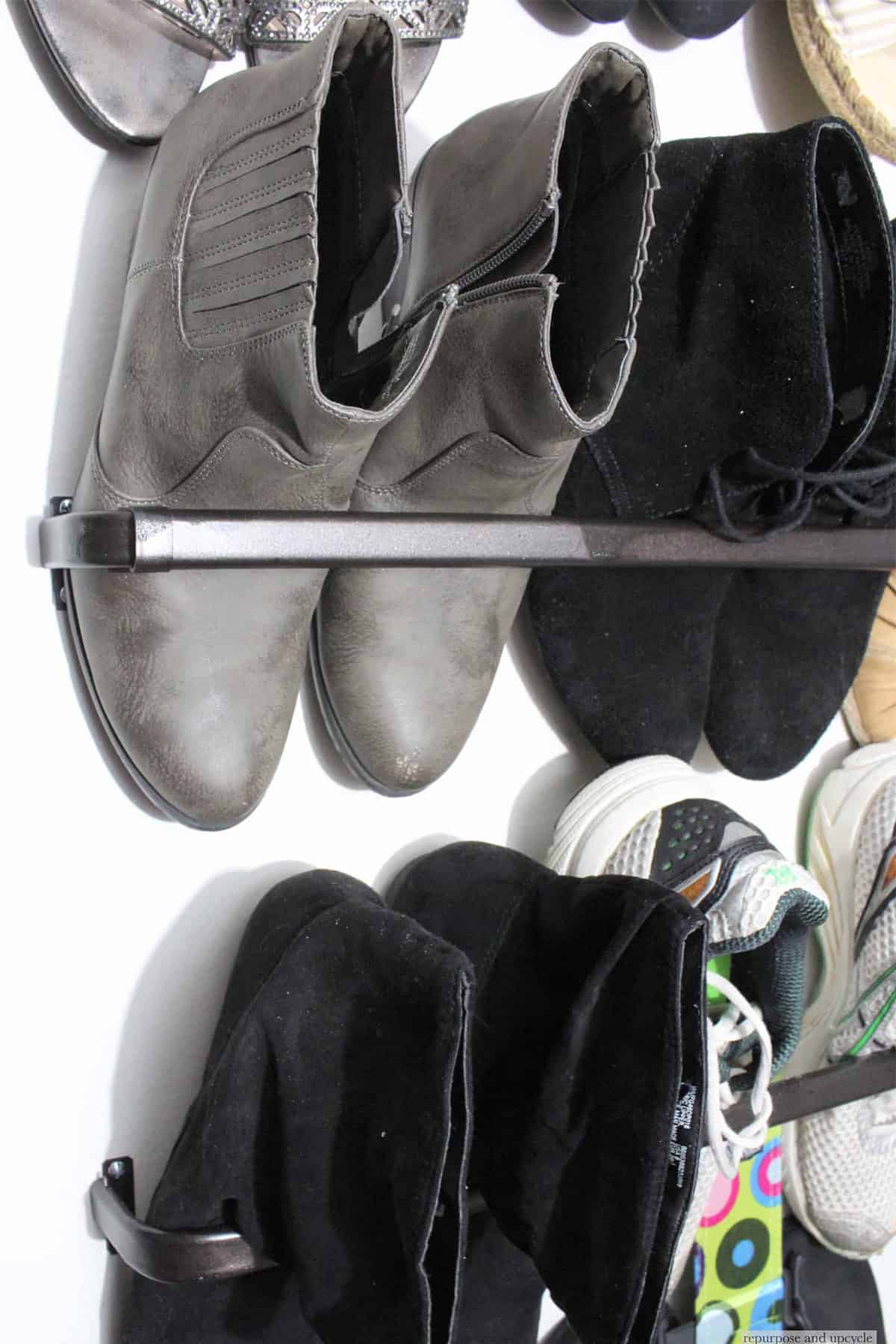 A series of shoes hanging in a closet on a curtain rod.