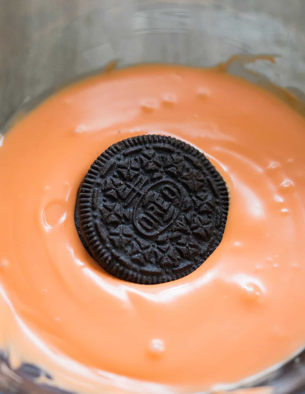 Oreo in orange tinted white chocolate in glass bowl for making basketball cookies.