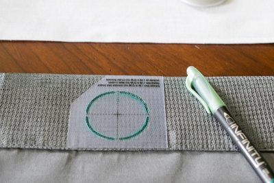 A curtain grommet template placed over a curtain with a marker drawing on the template.