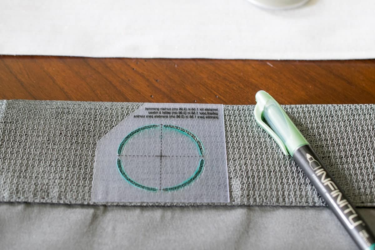 A curtain grommet template placed over a curtain with a marker drawing on the template.