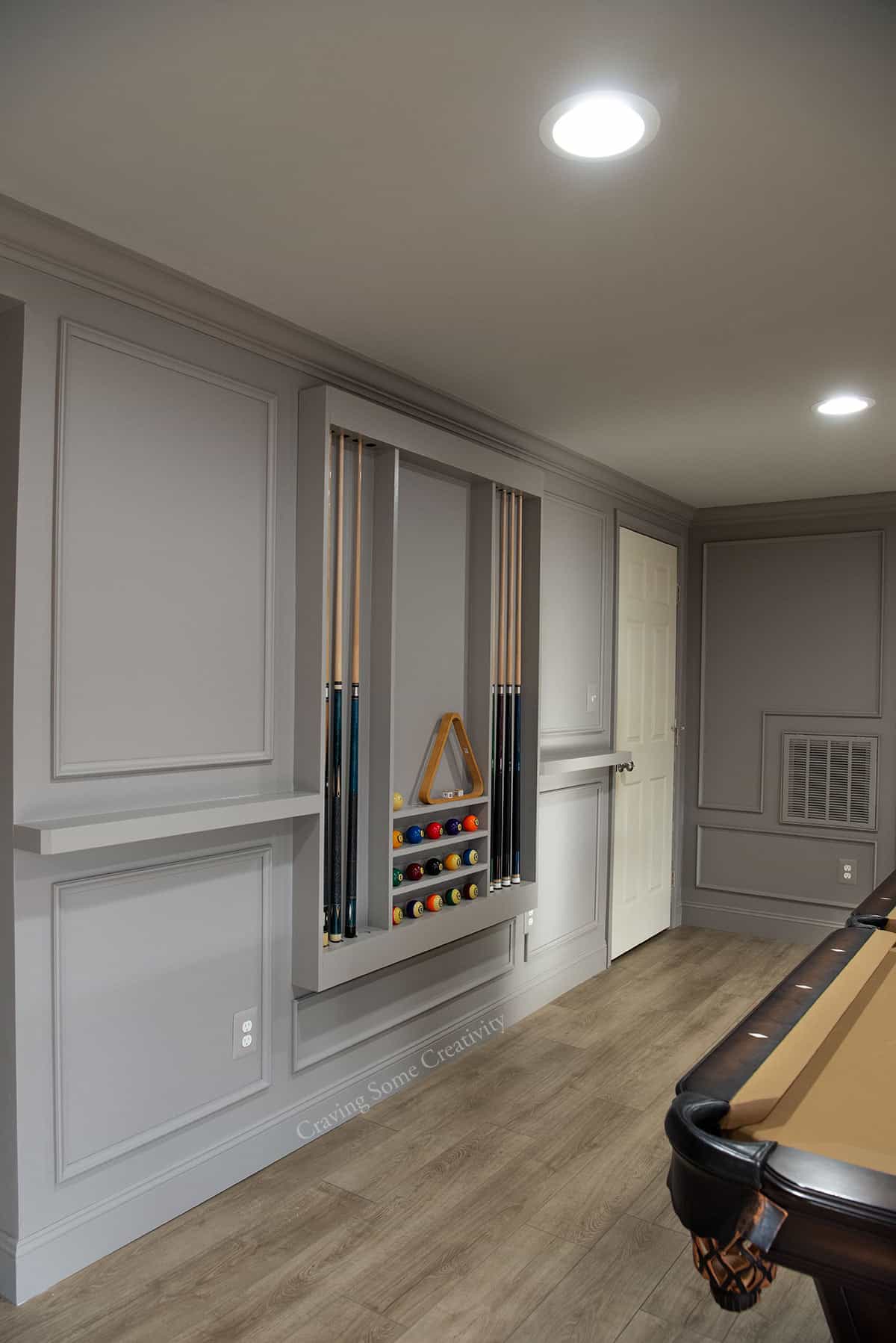 Basement wall with traditional box frame molding and a pool rack built into the wall and color drenched.