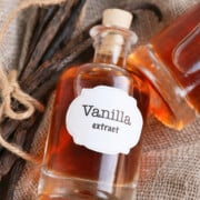 A bottle of homemade vanilla extract laying on burlap with vanilla bean pods next to it.