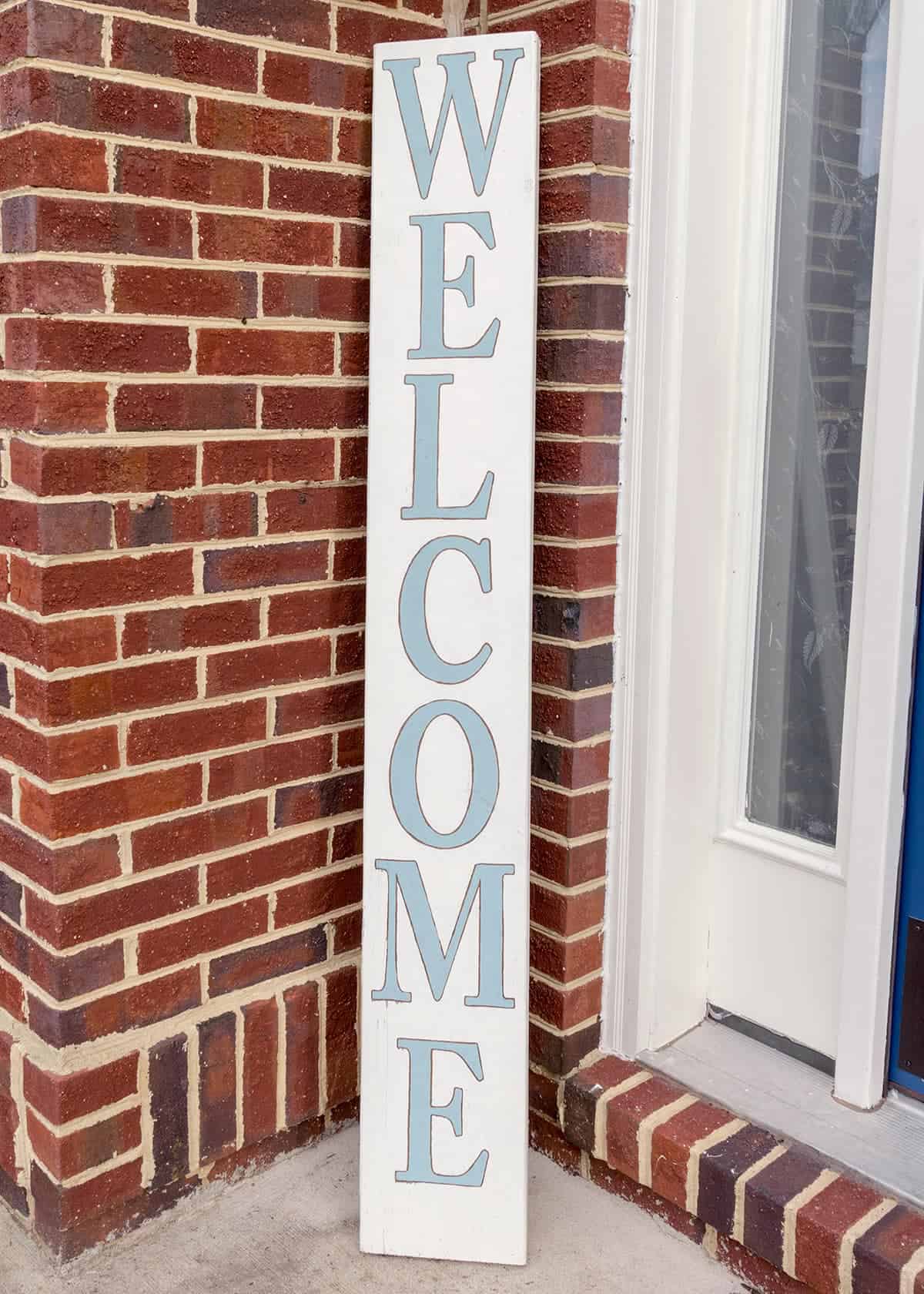 DIY wood welcome sign on the front porch with sky blue lettering.