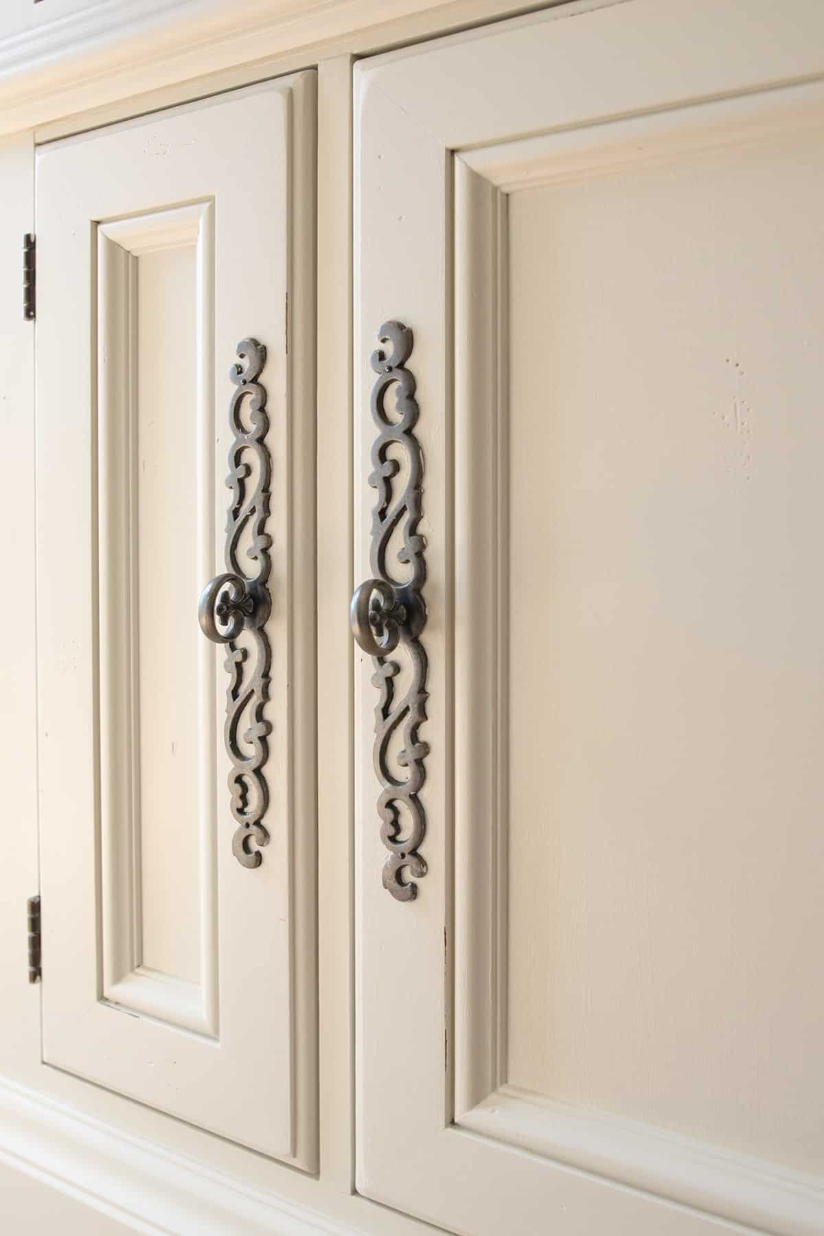 Closeup of ornate metal door handles on a white entertainment center console and bookshelves.