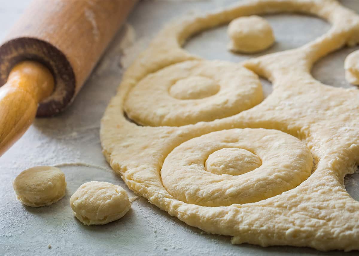 Dough on floured surface with donut shapes cut out.