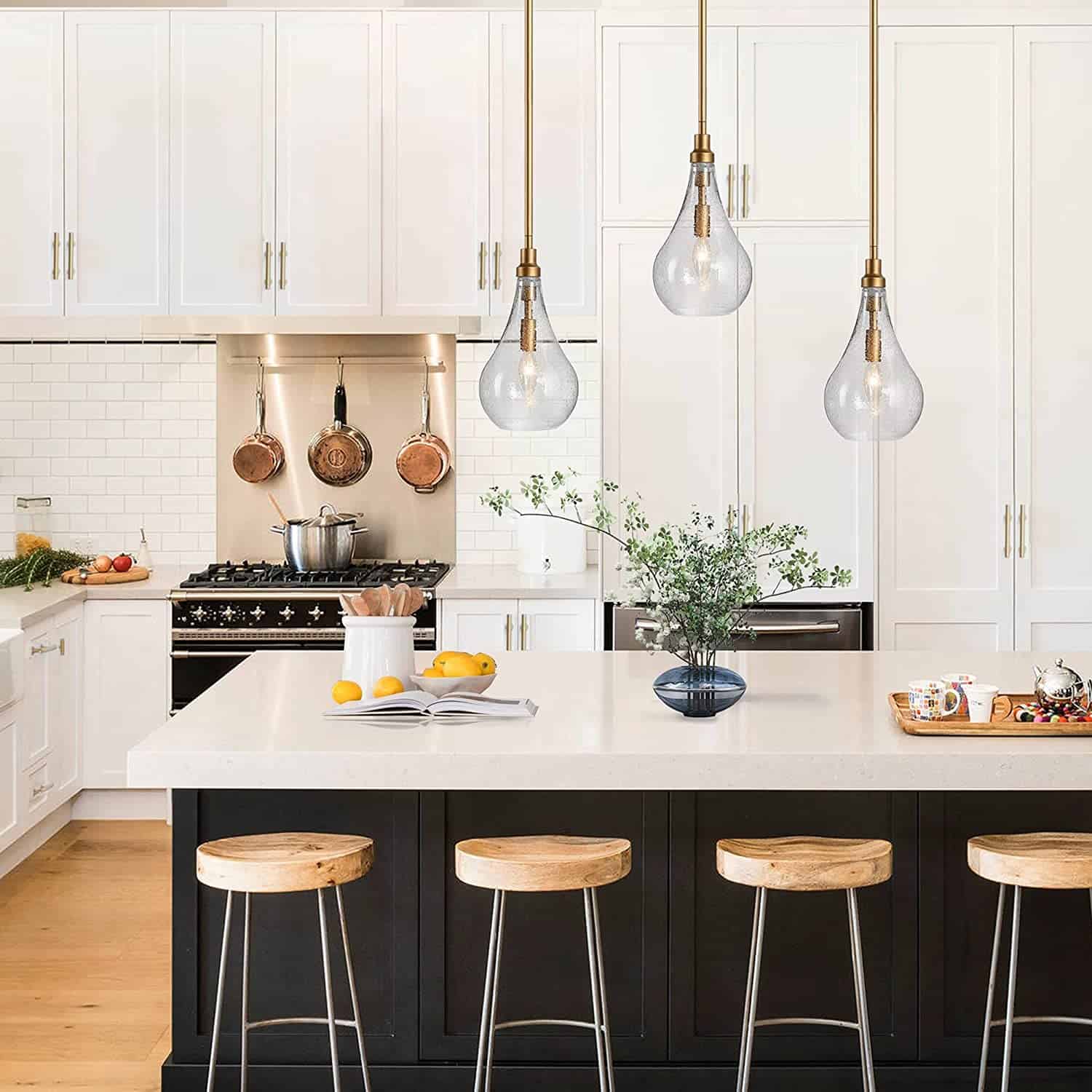 Three glass pendant style light fixtures with brass hardware over white and black island in modern traditional kitchen.
