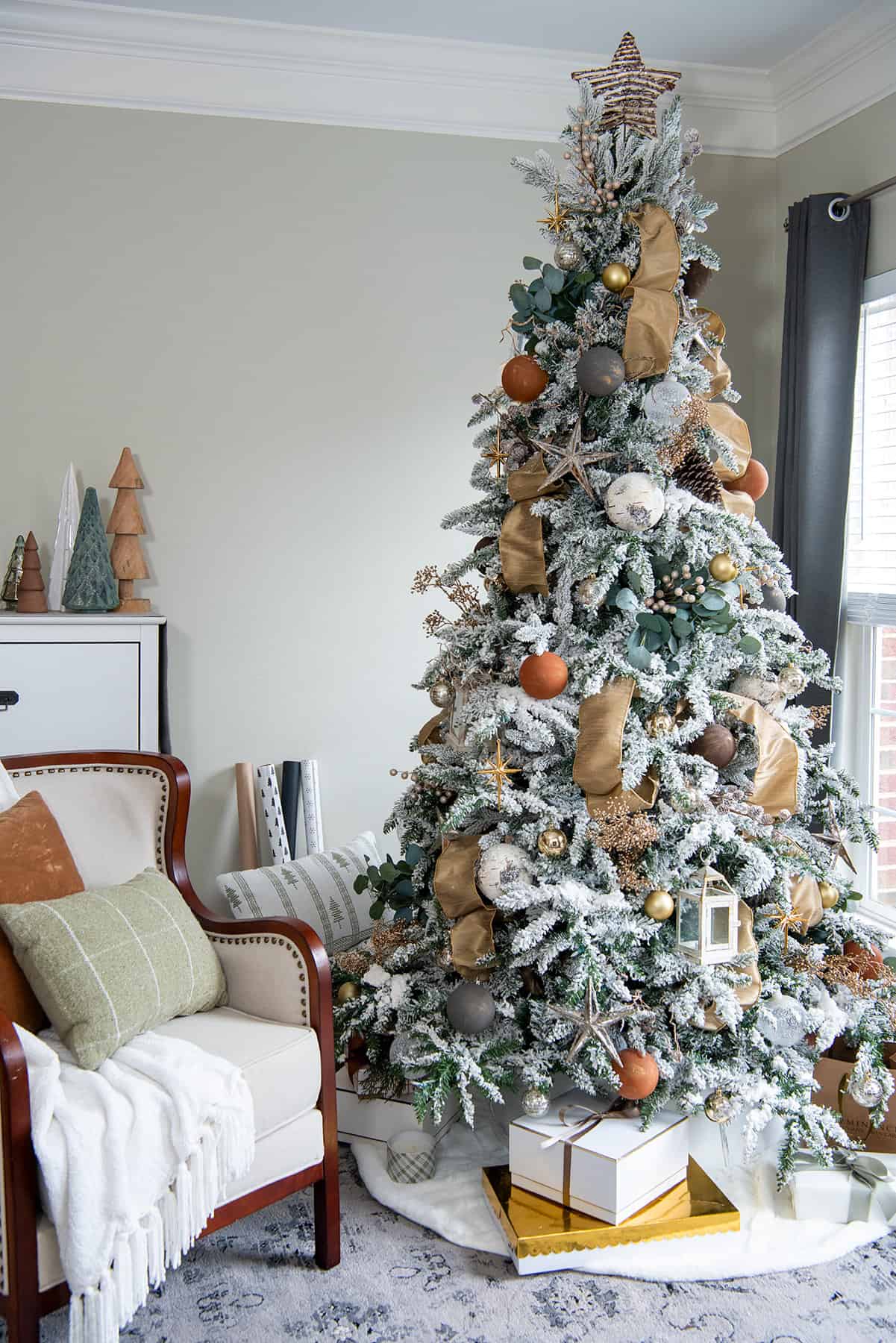 Natural Christmas tree with earth tones decorations and a chair next to it.