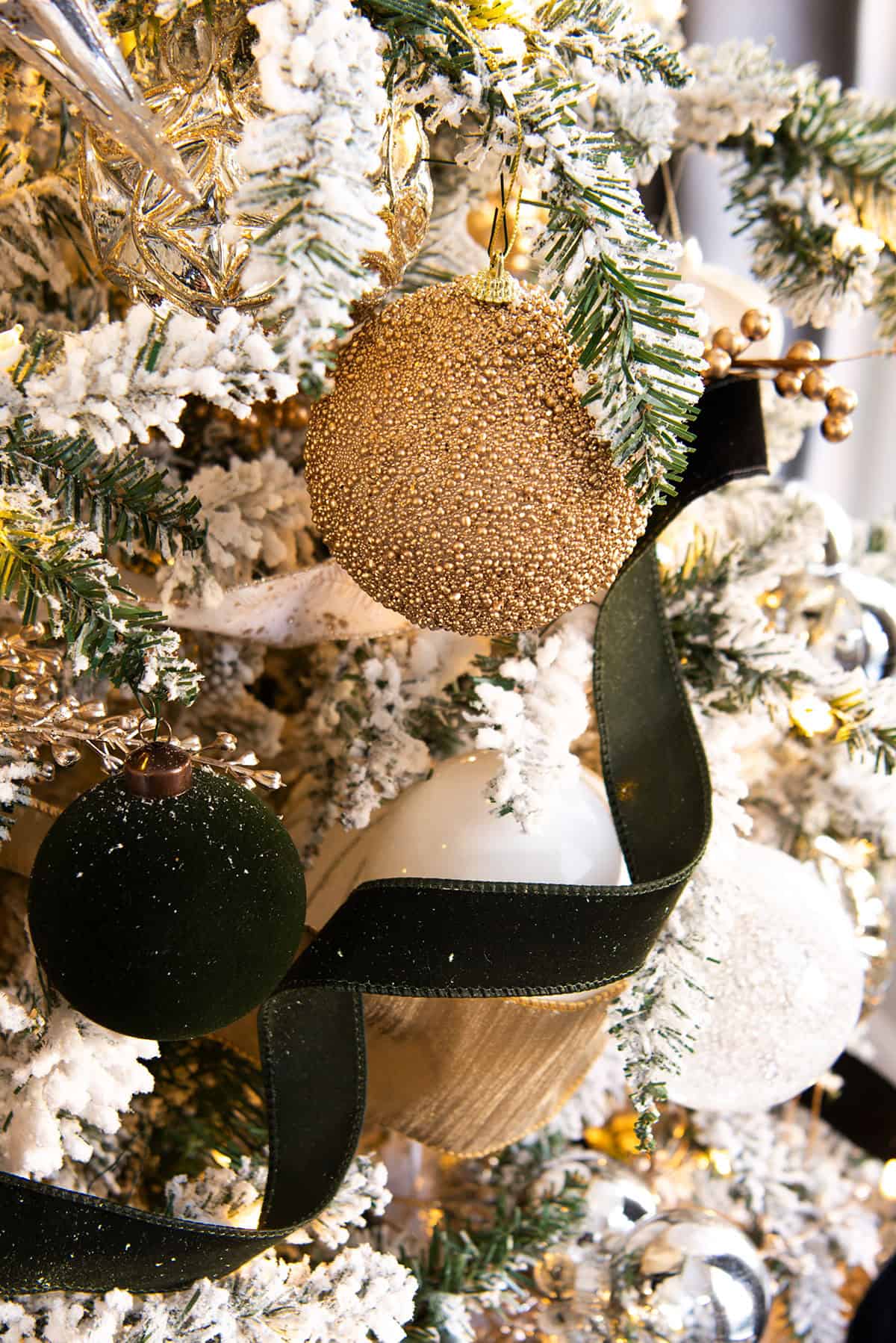 Closeup of a gold beaded ornament with black and white ribbon on a flocked tree.