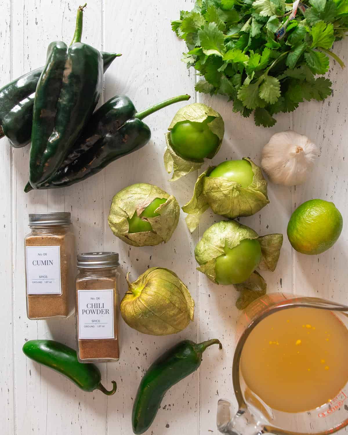Ingredients for tomatillo sauce for enchiladas including tomatillos, cilantro, peppers, chicken broth, cumin, and chili powder.