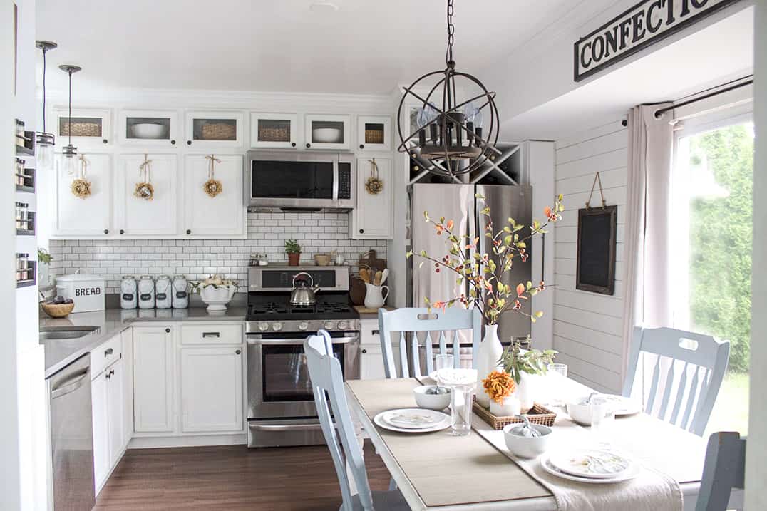 White farmhouse style kitchen with extended row of high glass-door cabinets and built in storage.