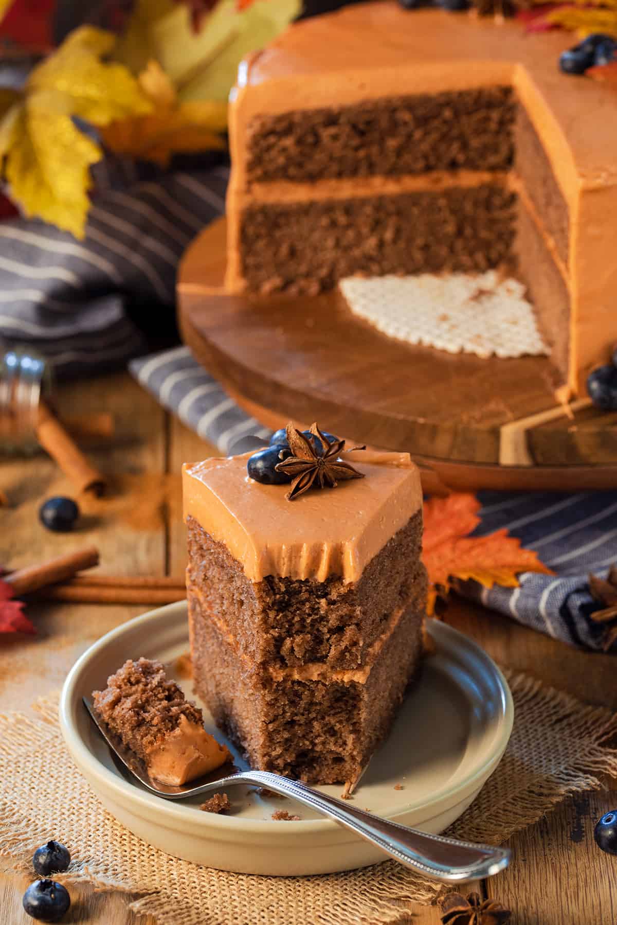 A slice of layer cake on a plate in front of the cut cake on a cake stand.