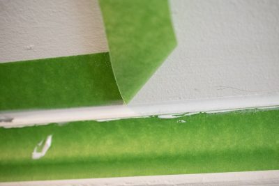 Painter's tape being carefully pulled up to reveal a clean edge of caulk.