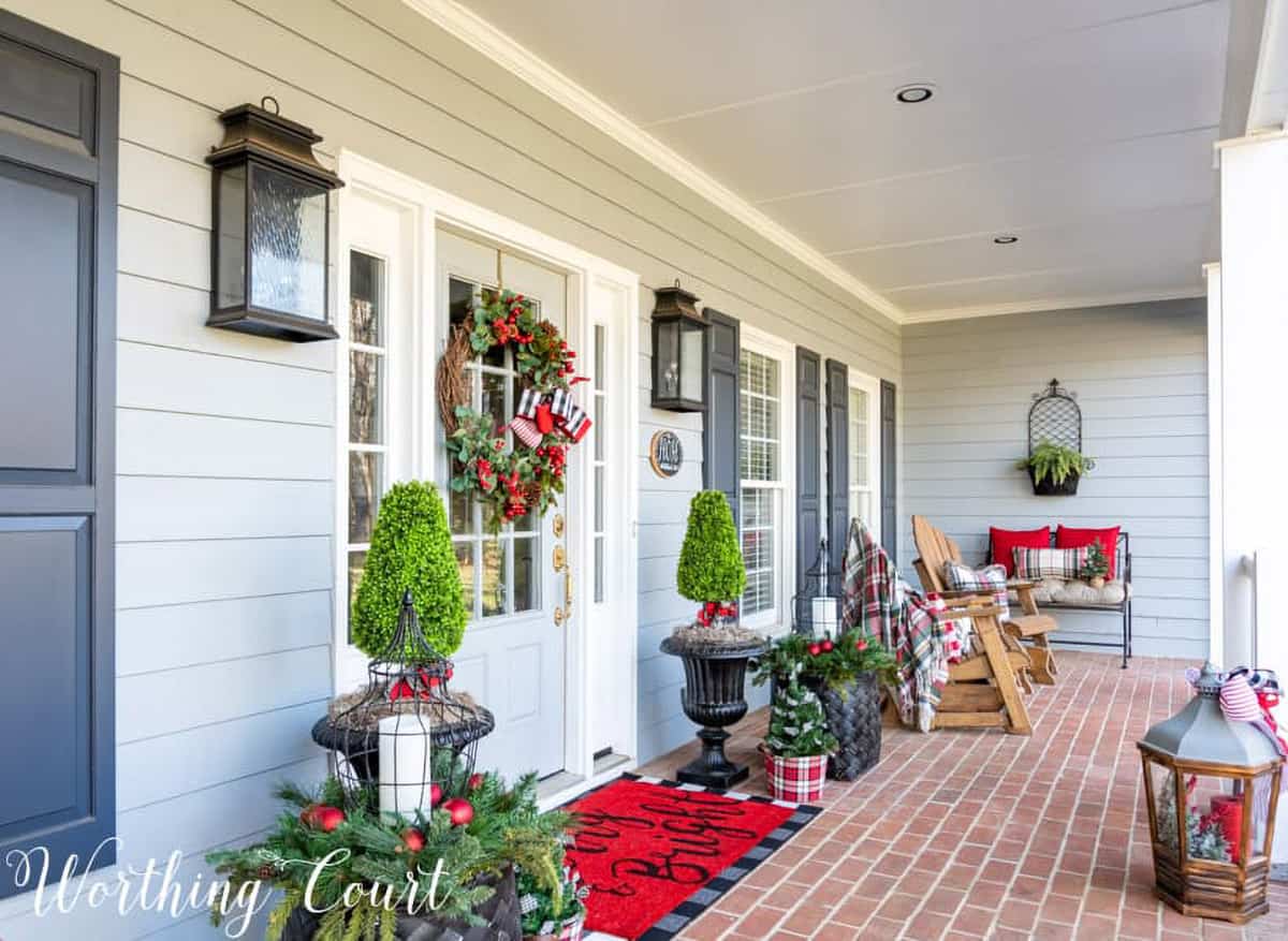 Large, covered porch with red and green holiday decorations like lanterns, plaid, and topiaries.