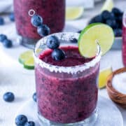 Blueberry margarita in a rocks glass with a salt rim and lime wheel.