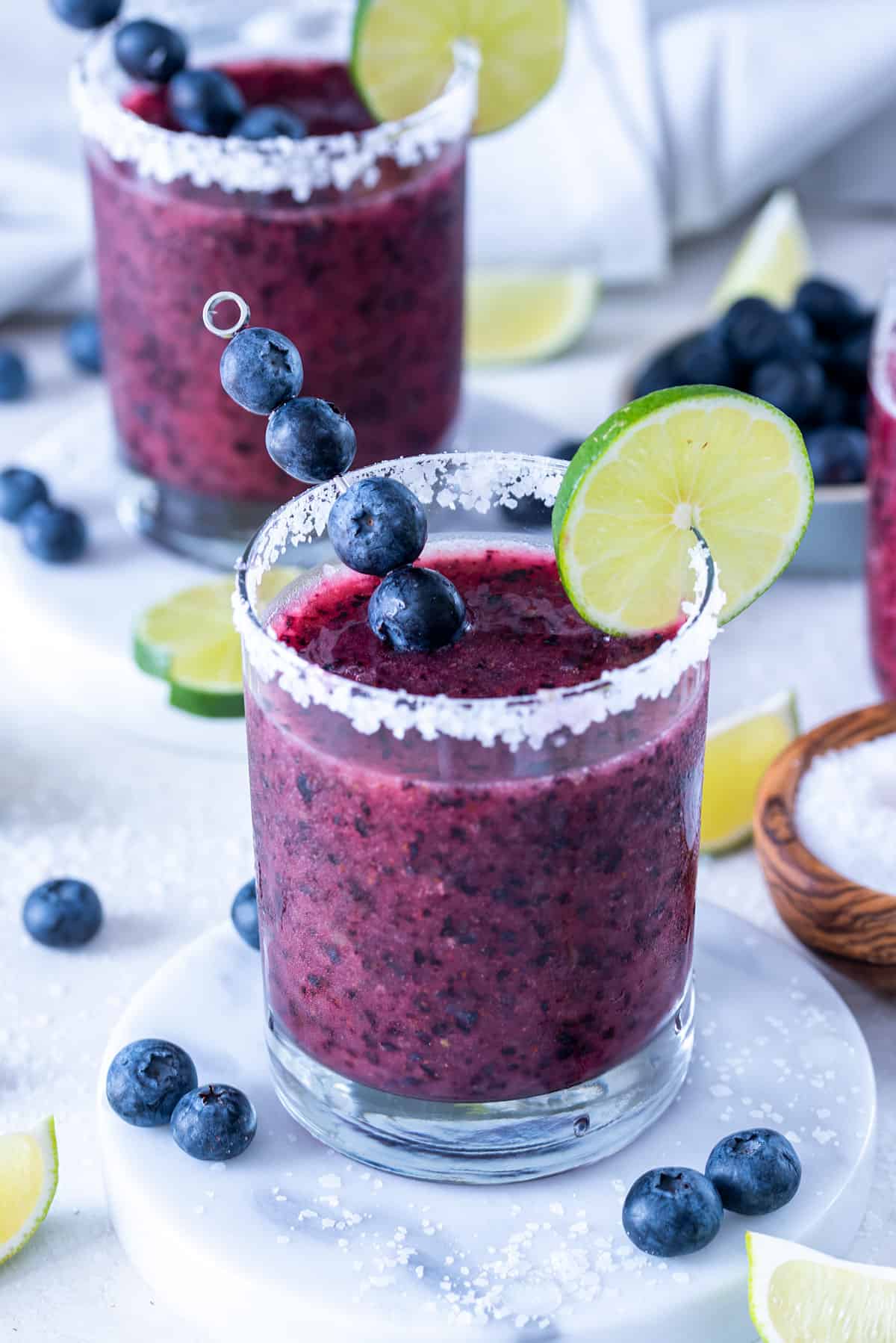 Blueberry margarita in a rocks glass with a salt rim and lime wheel.