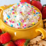 A bowl of cake batter dip with brightly colored sprinkles on top and strawberries and animal crackers around the bowl.