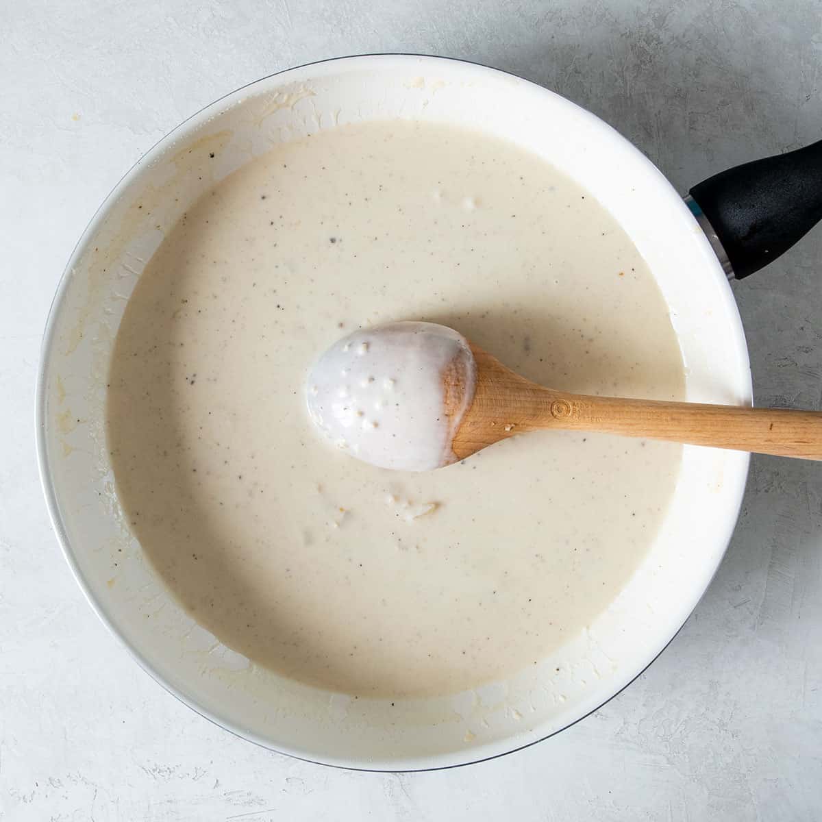 Prepared garlic cream sauce in a skillet with a wooden spoon inside to show the texture of the sauce.