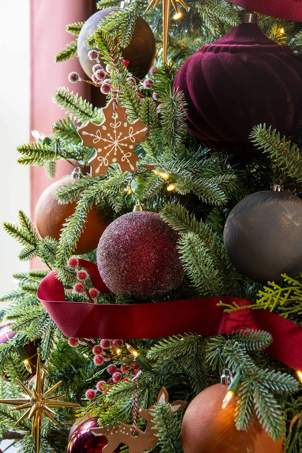 Burgundy and gingerbread ornaments on an evergreen tree with a Victorian inspired decor.