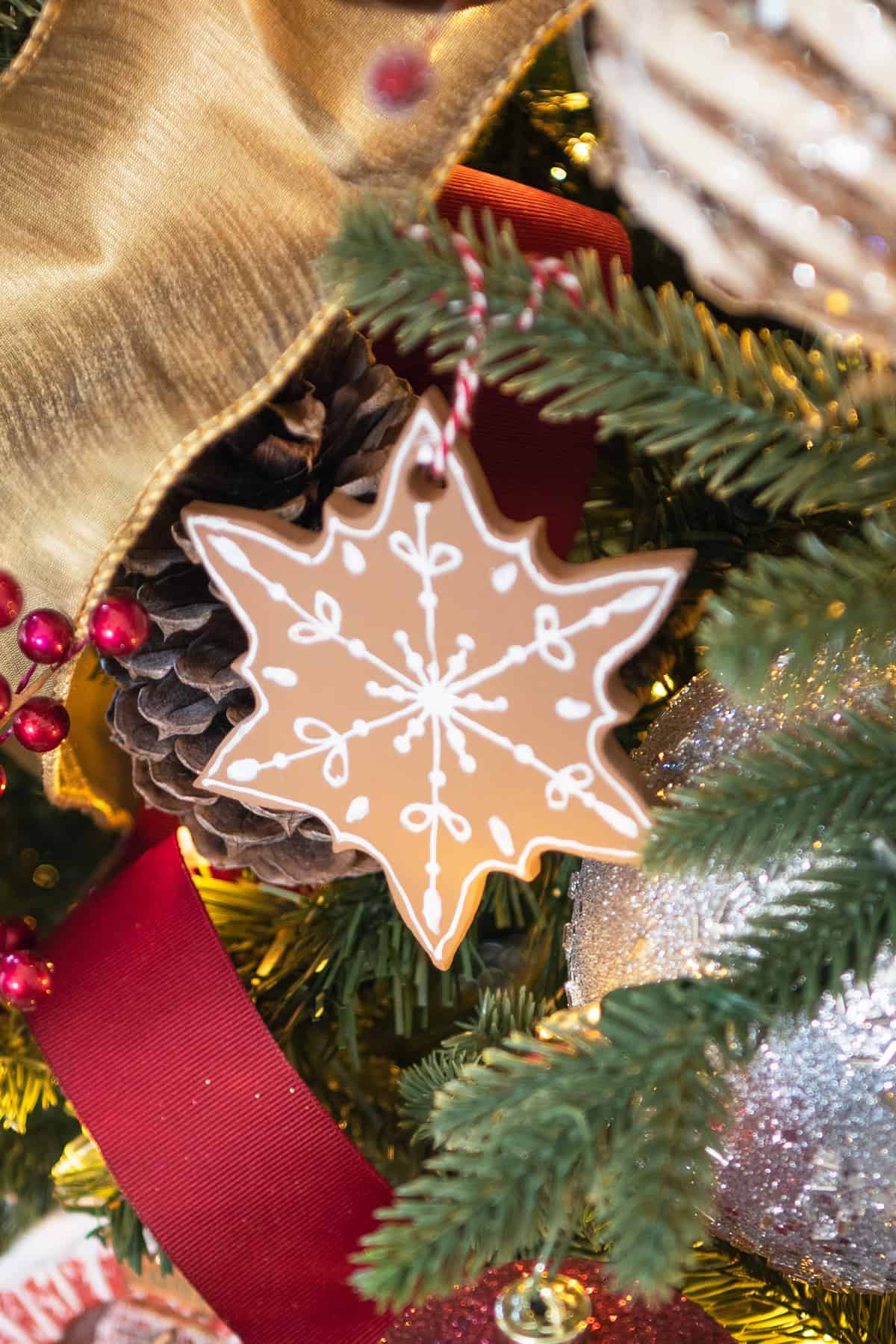 Snowflake gingerbread ornament on tree that looks like a cookie surrounded by red and gold ribbon.