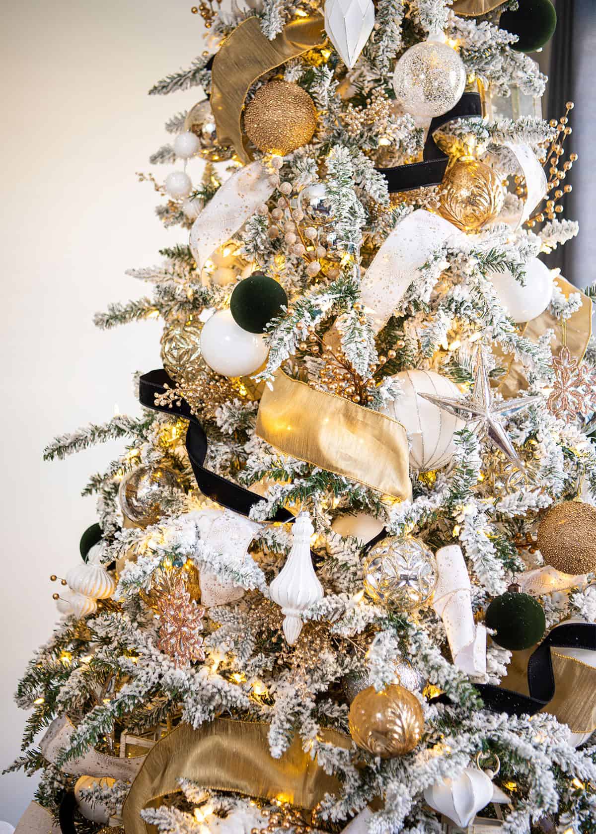 Flocked christmas tree with black and white and gold ornaments on it.
