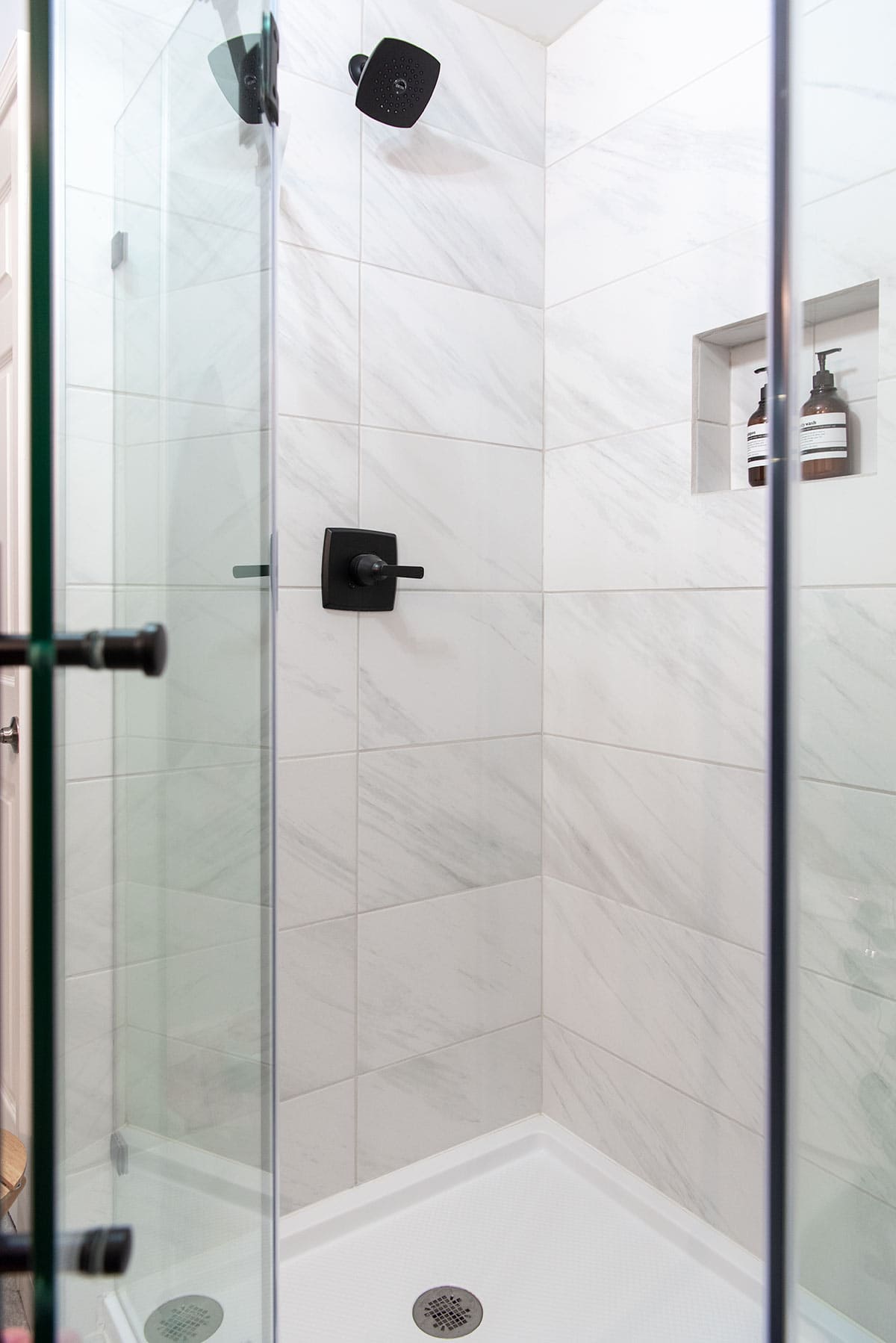 A peek into a white marble shower with black fixtures and modern glass doors.