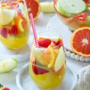 A glass of green apple sangria on marble coaster with pitcher and glasses in the background.