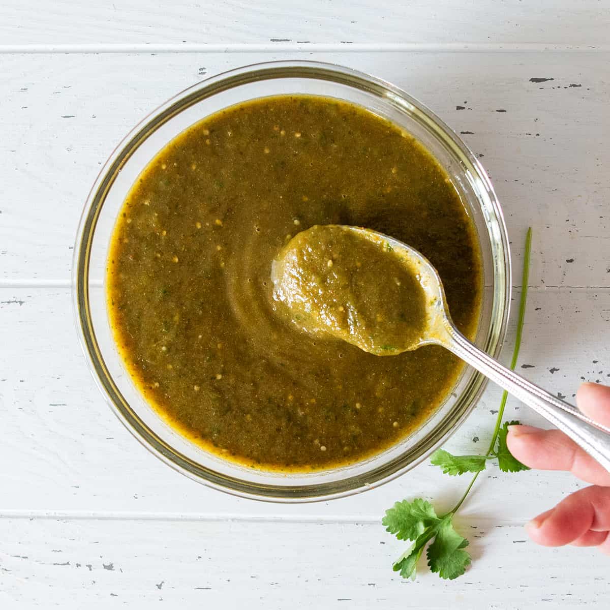 Overhead of a bowl of green enchilada sauce with a spoon in it.