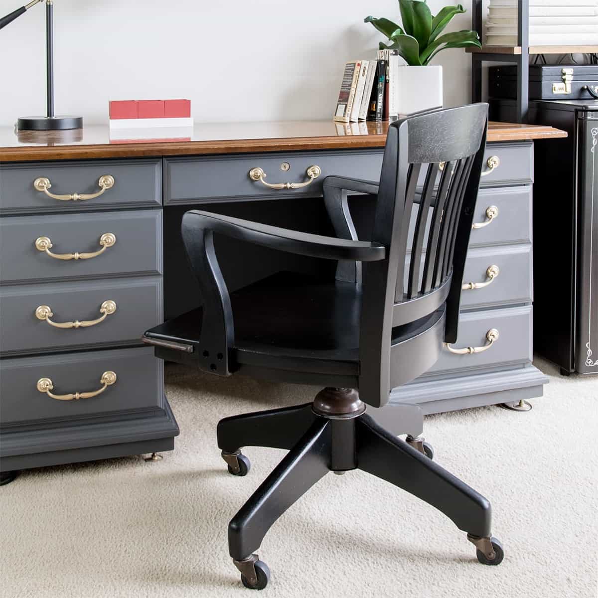 Black office chair in front of gray vintage desk with brass hardware after makeover.