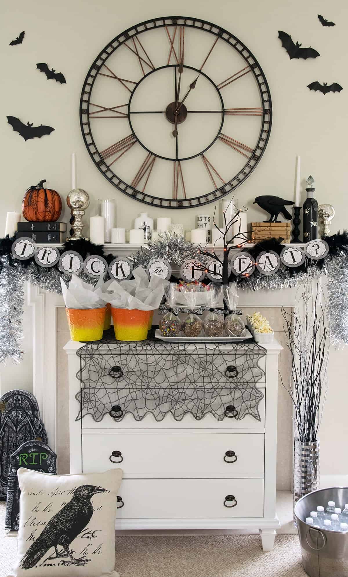 Spooky Halloween mantle with dessert buffet in front. Decorations include ravens, gravestones, a clock, and candles.