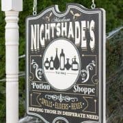 Halloween yard sign with witch's apothecary shop motif hanging on a frame.