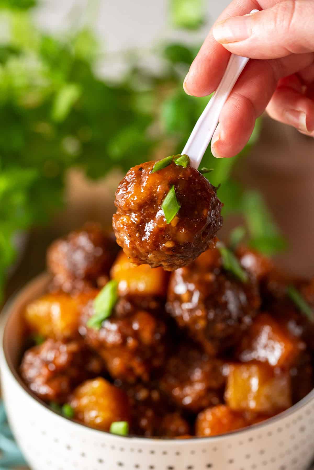 Single Hawaiian meatball on a toothpick held in front of a bowl.