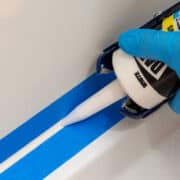 Closeup of a woman caulking a shower surround using painter's tape.