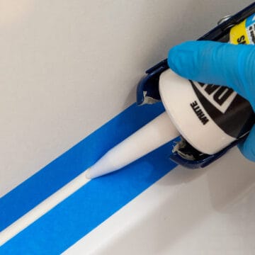 Closeup of a woman caulking a shower surround using painter's tape.