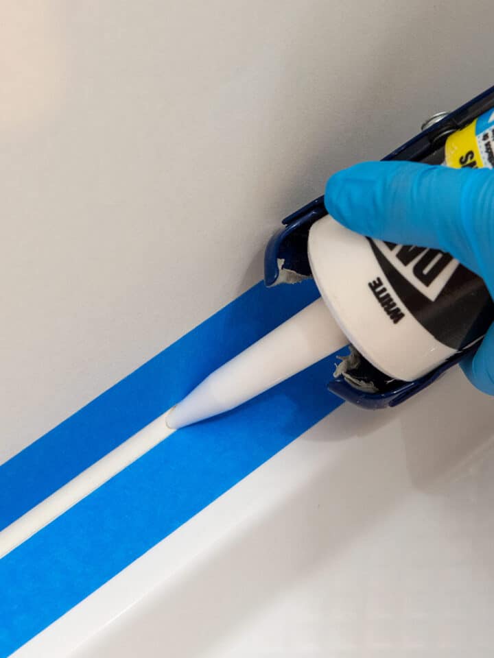 Closeup of a woman caulking a shower surround using painter's tape.