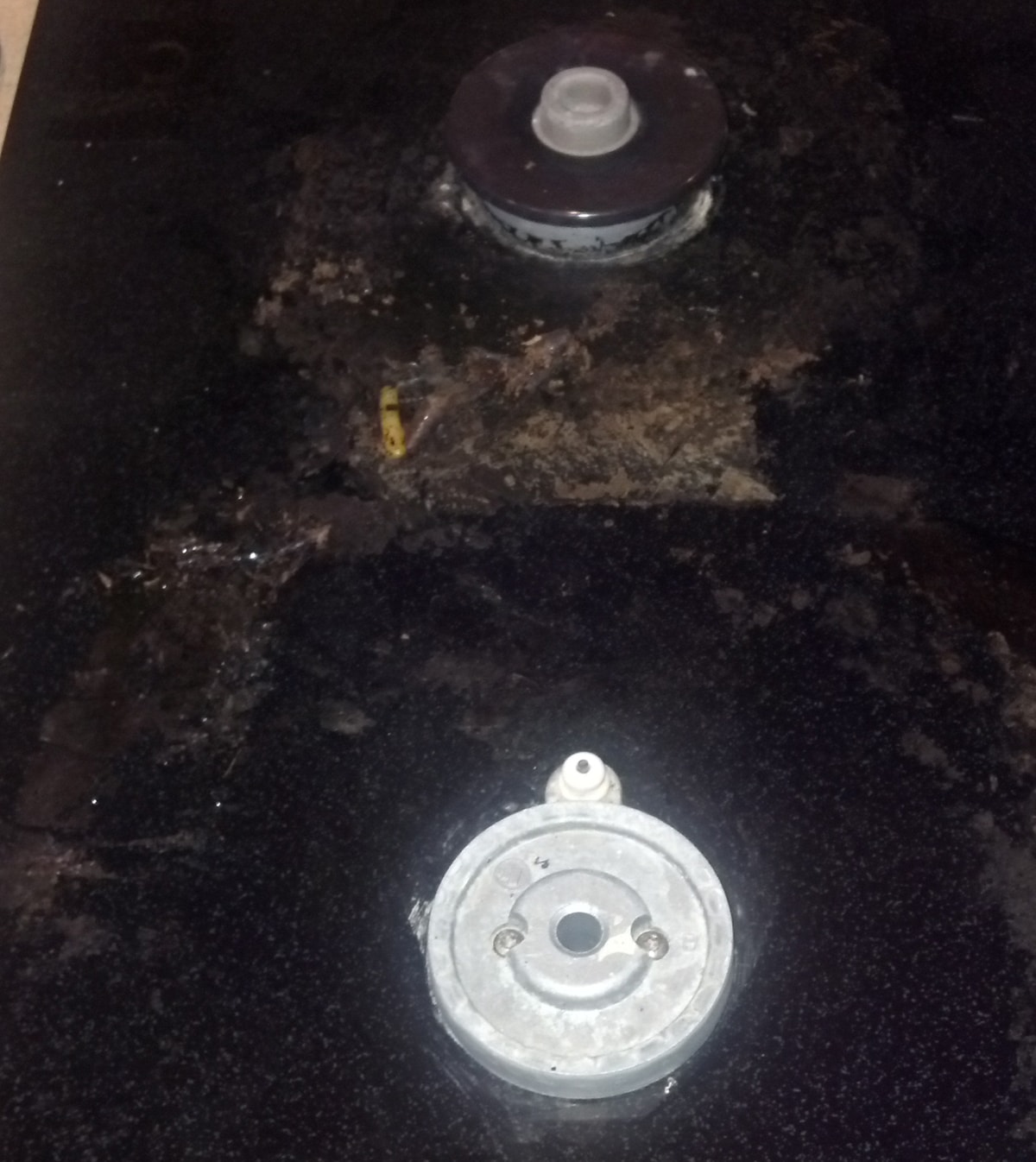 Dirty and damaged surface of a black glass stove and burner.