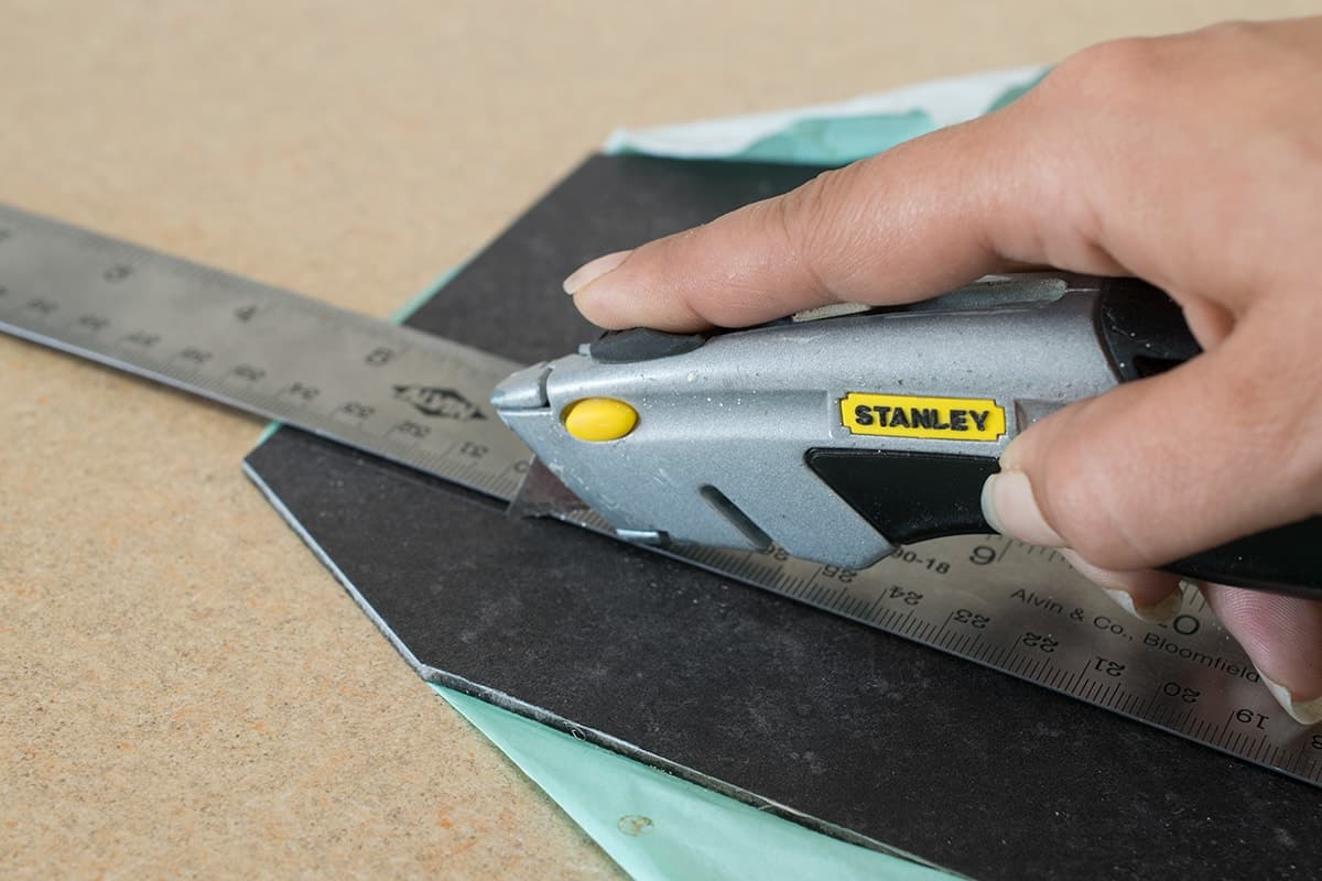 Woman cutting luxury vinyl tile with a razor blade and straight edge.