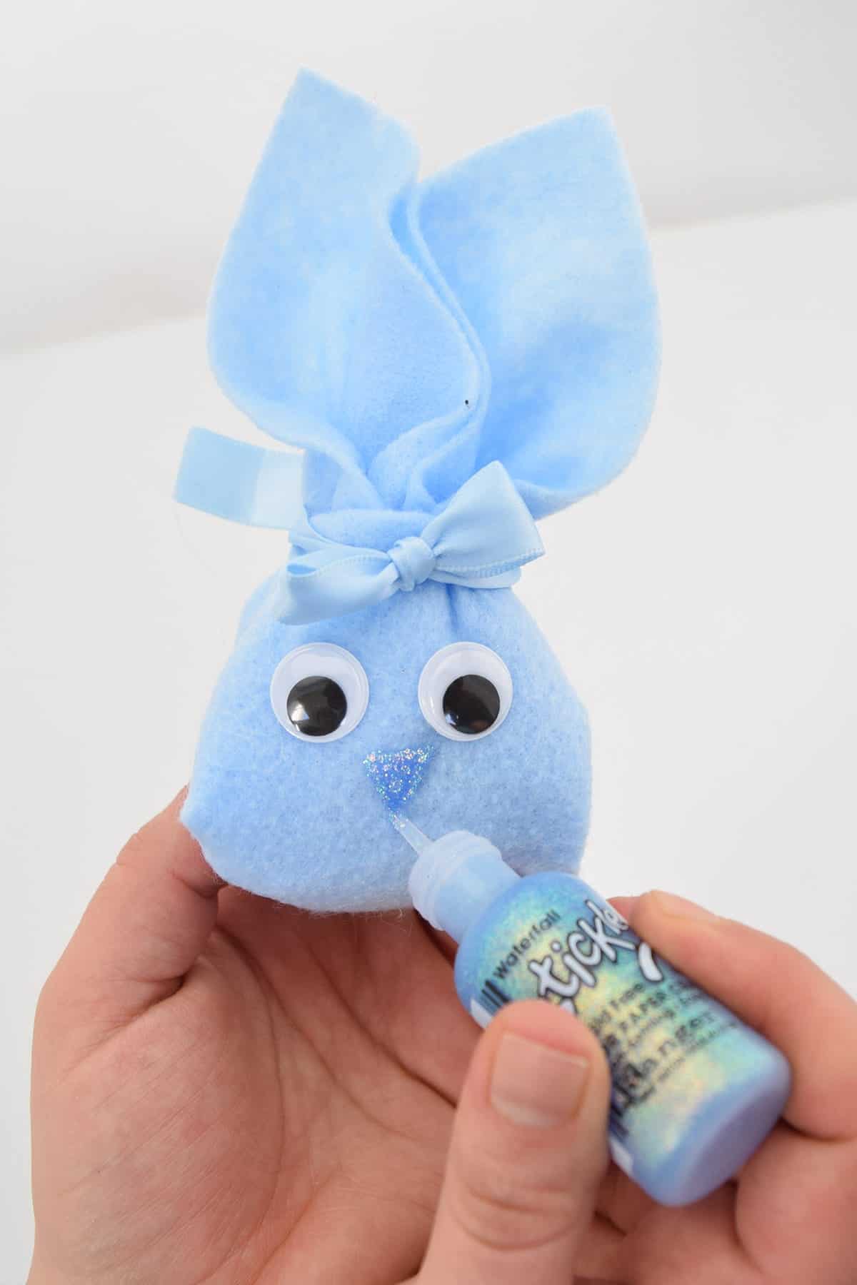 DIY blue felt bunny pouch with googly eyes held in hand painting glitter nose and mouth on front.