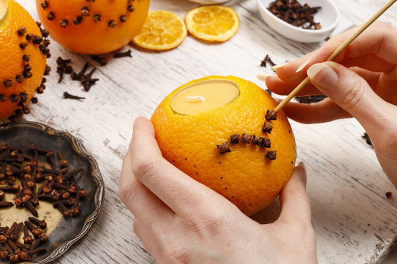 Woman poking orange with clove to make a pomander ball.
