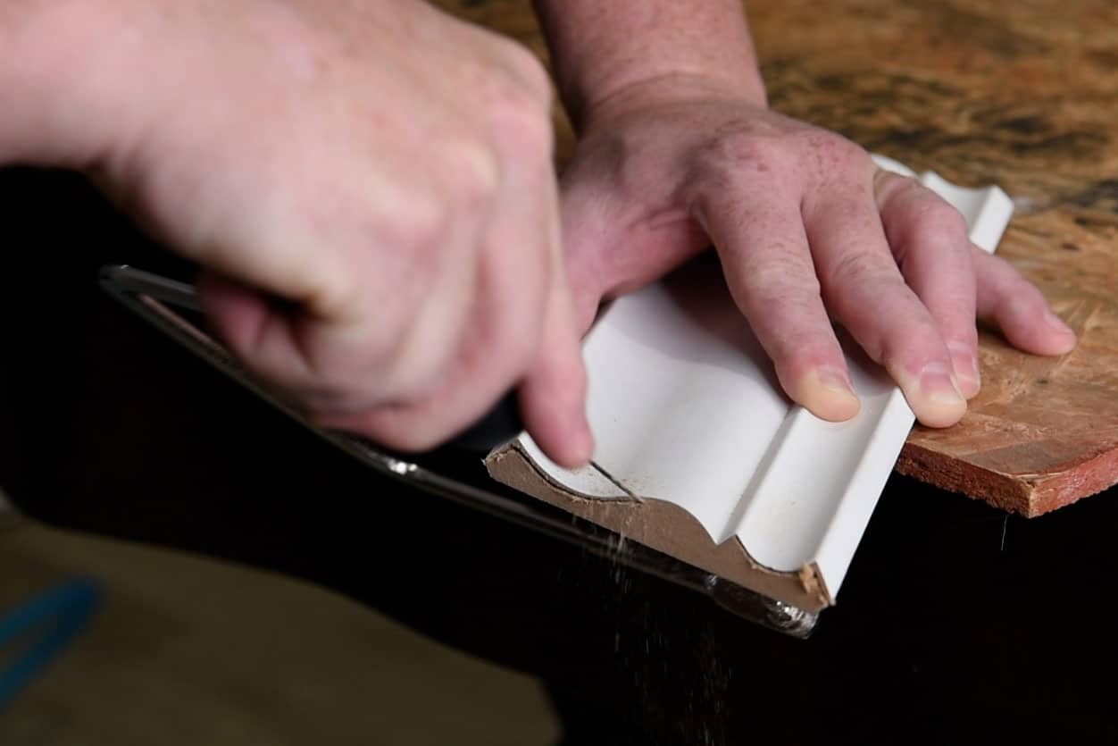 Man coping a piece of crown molding at an angle.