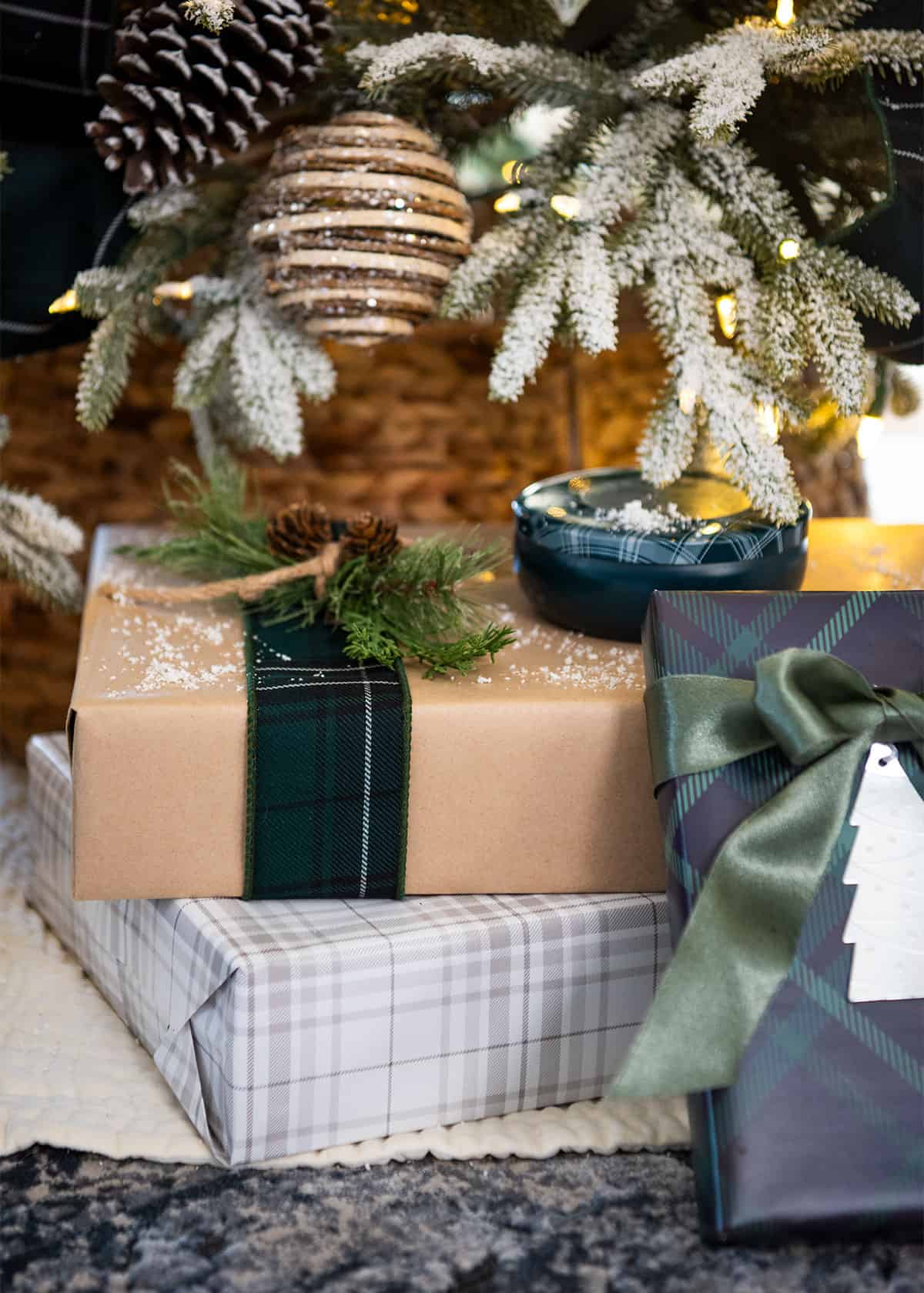 A grouping of presents under the tree. The presents are decorated with hunter green ribbon, blue plaid wrapping paper, and craft paper.
