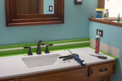 How To Caulk around a vanity. Image depicts new vanity top and tools required, taping technique.