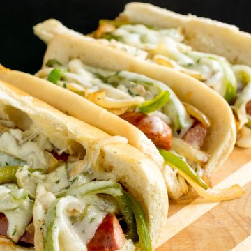 Kielbasa sandwiches with hoagie buns onions and peppers on a butcher block.